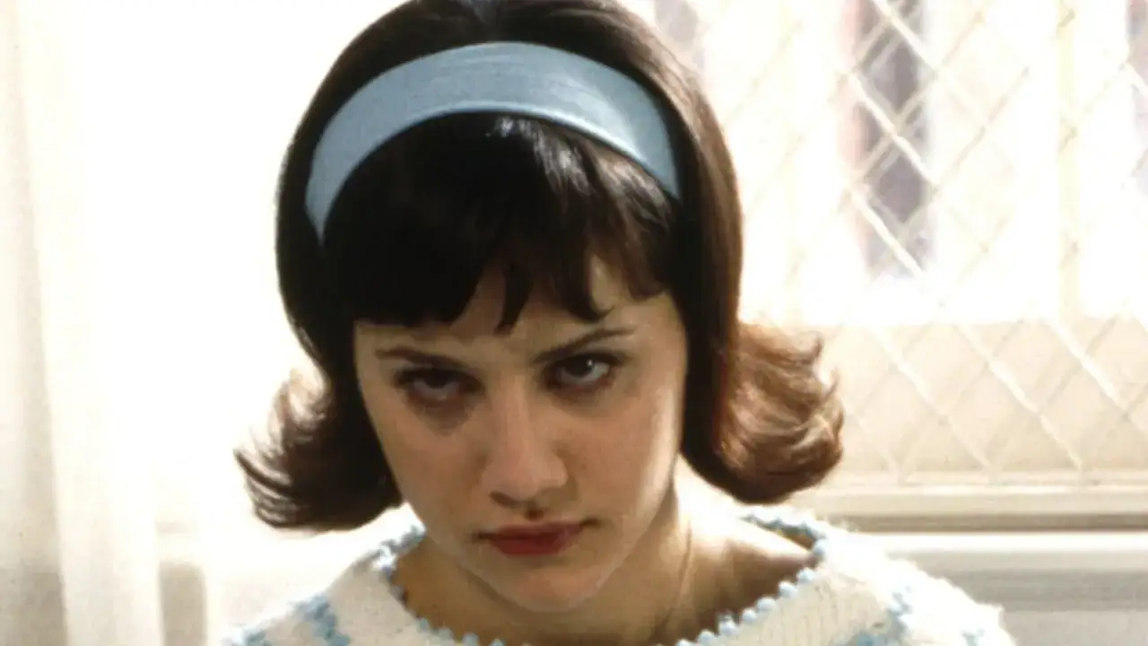 Brittany Murphy w filmach, z niebieską opaską na włosach i w sweterku, patrzy z determinacją.