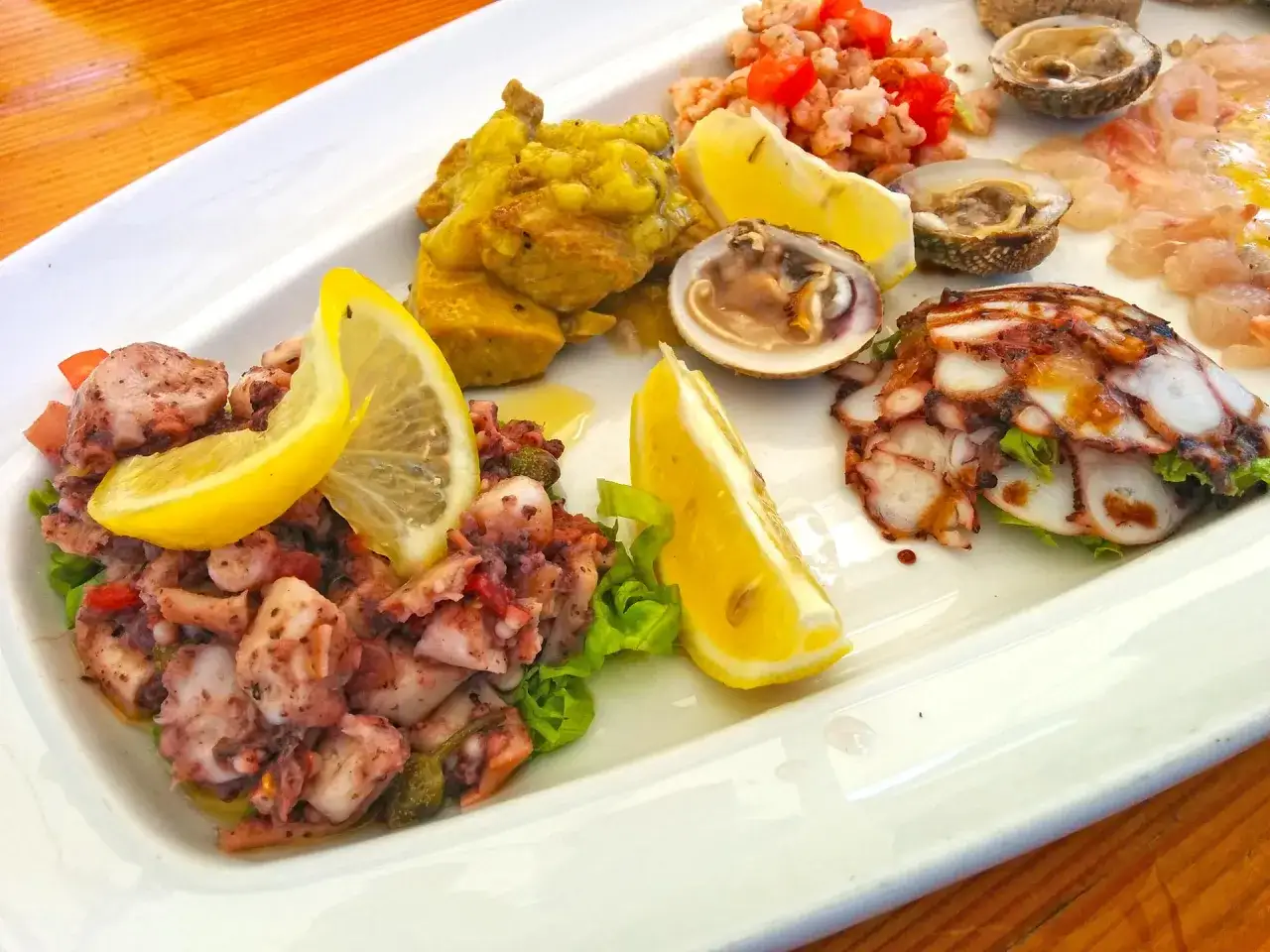 Pyszne chorwackie jedzenie: sałatka z ośmiornicy, krewetki, małże i carpaccio z ryby, ozdobione cytryną.