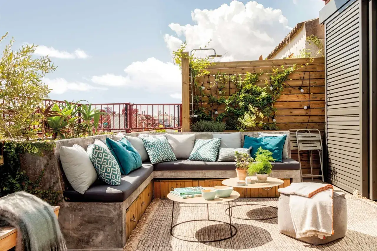 Sofá de hormigón con cojines turquesas y verdes, mesas bajas y plantas. Ideas para jardineras exteriores con estilo moderno.