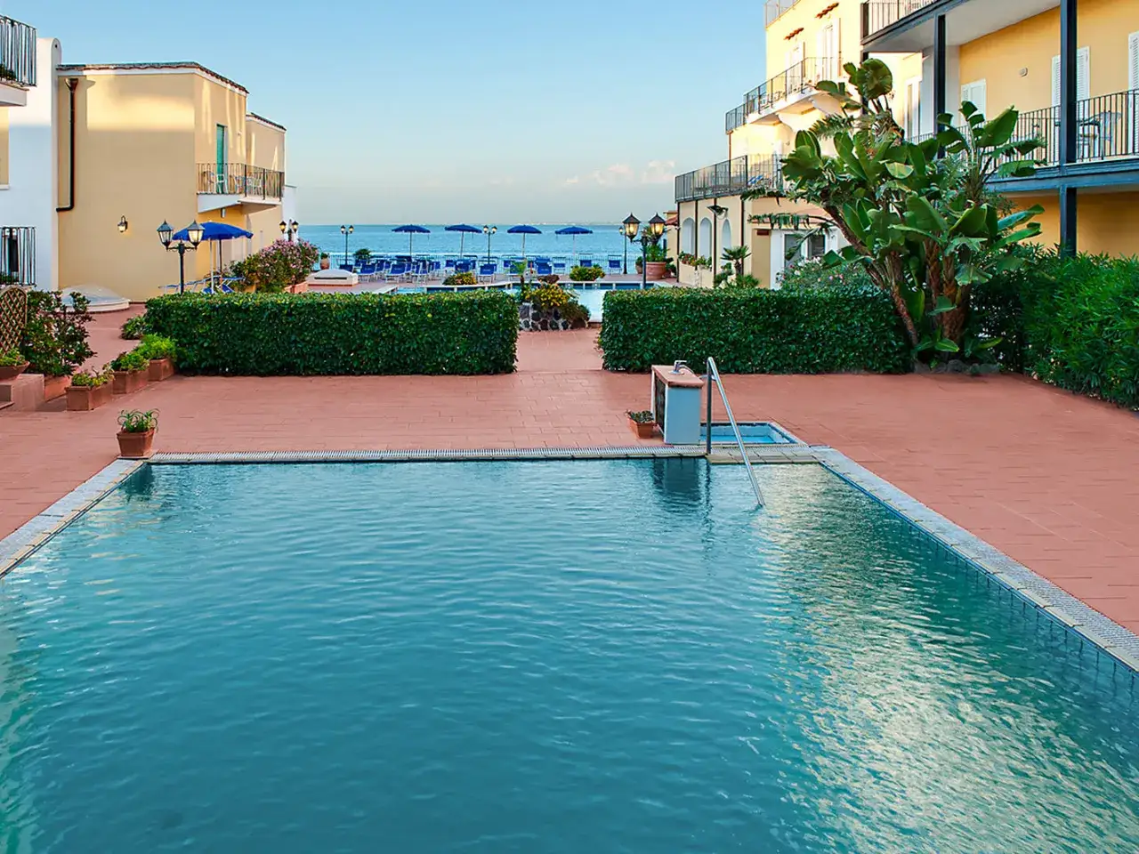 Piscina e mare al **hotel Parco Aurora Terme Ischia**. Ombrelloni blu e vegetazione lussureggiante invitano al relax.