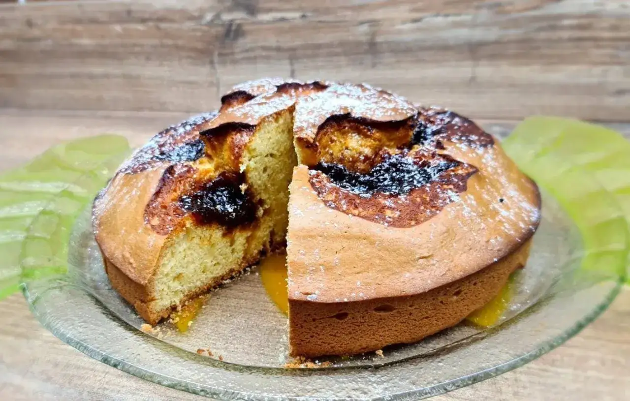 Torta soffice con marmellata scura e zucchero a velo, una fetta è stata tagliata rivelando il ripieno.