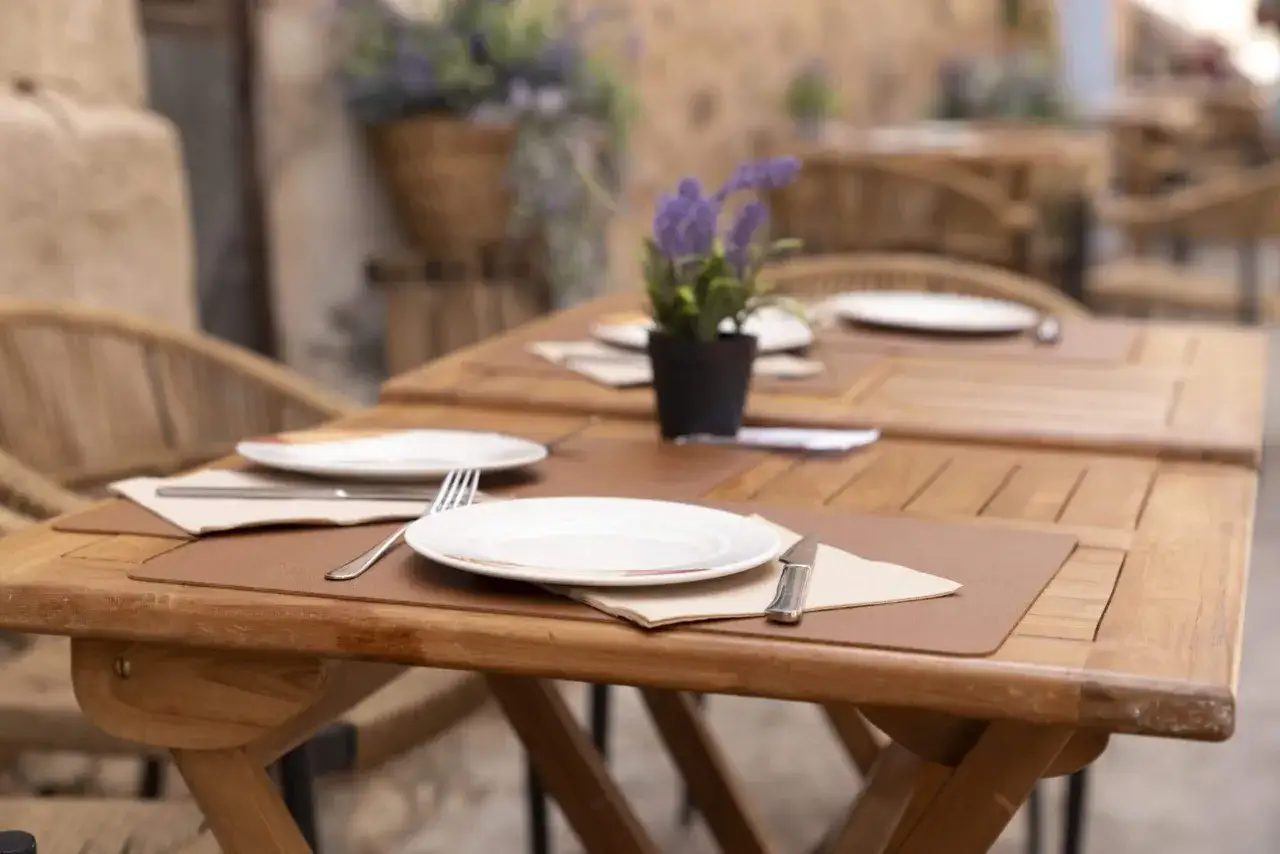Mesas de madera al aire libre, listas para disfrutar de d&oacute;nde comer en Albarrac&iacute;n. Flores moradas decoran el ambiente.