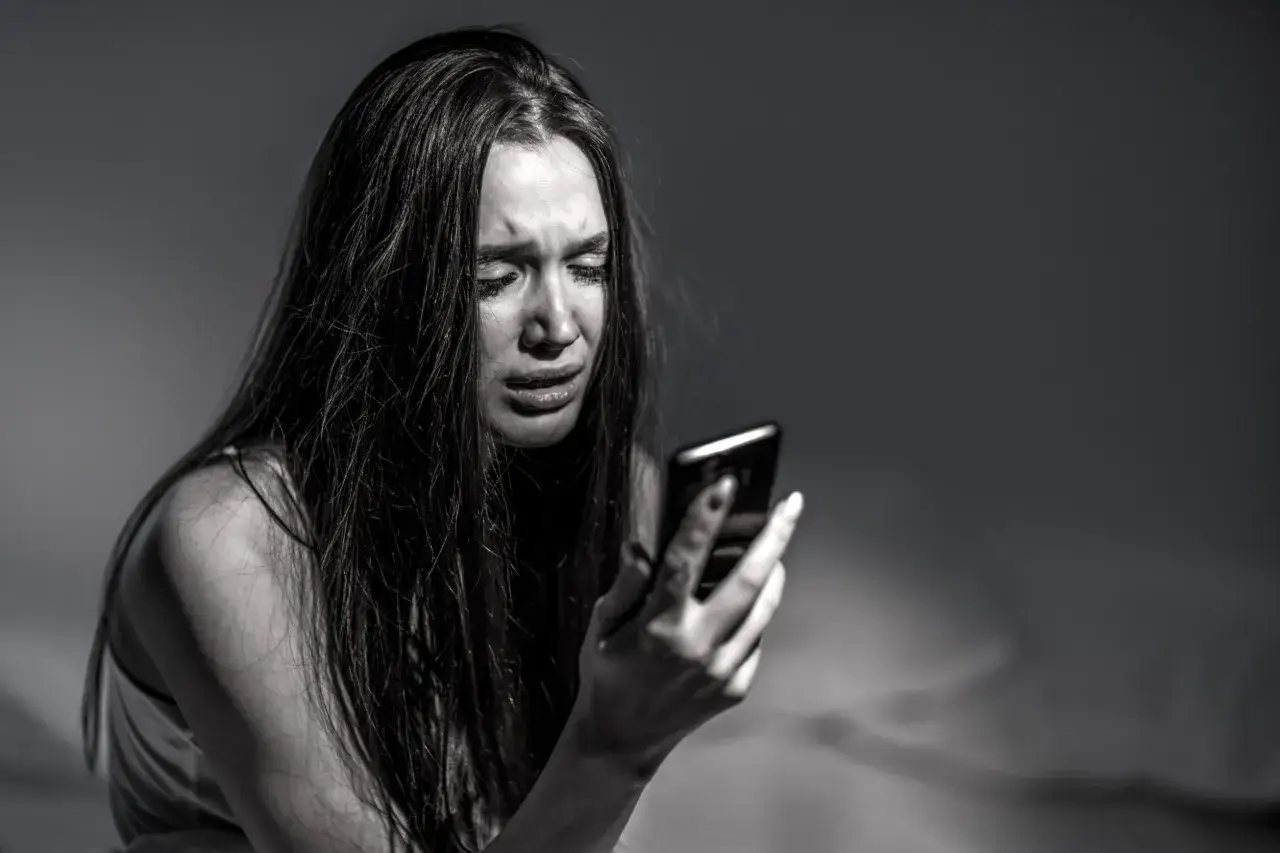 Ragazza piange guardando il telefono, forse a causa delle conseguenze del sexting.