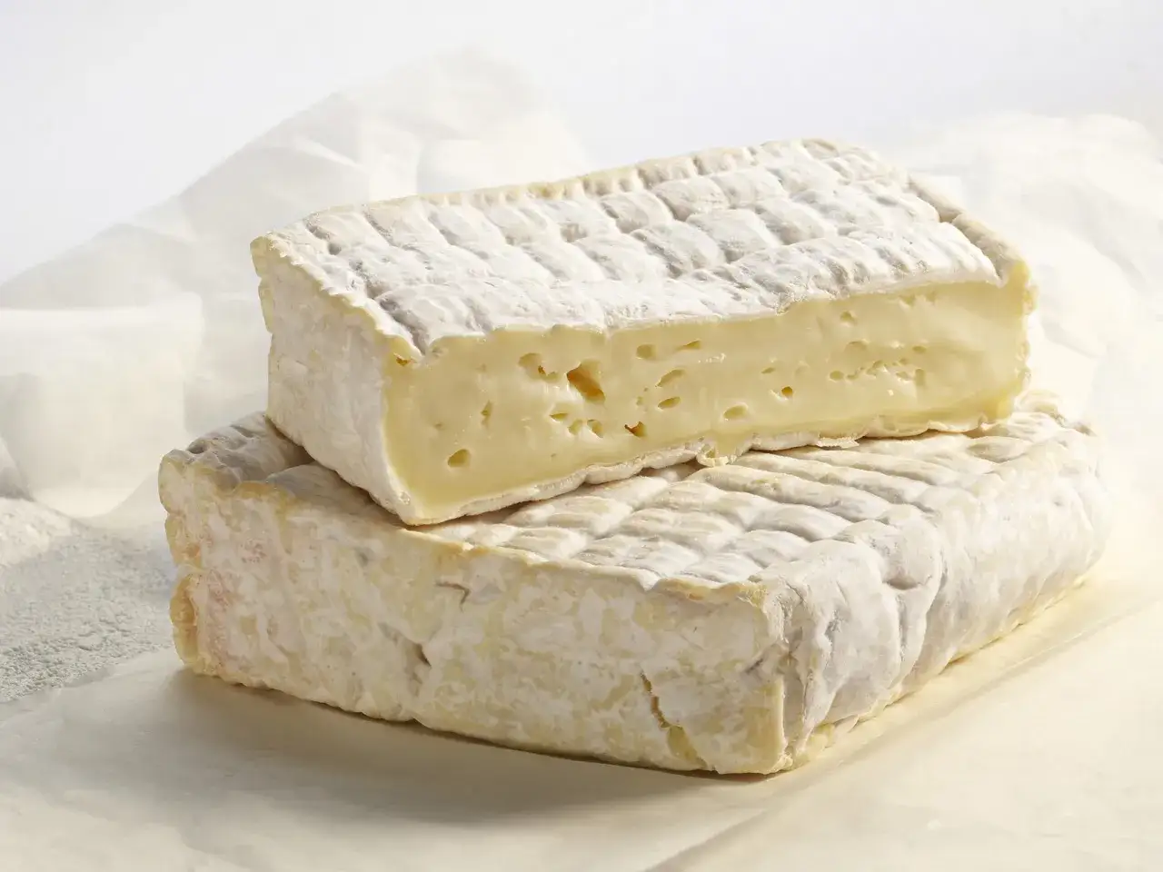 Deux blocs de Pont-l'Évêque, un fromage à pâte molle et croûte lavée, révèlent leur texture crémeuse et leur goût unique.