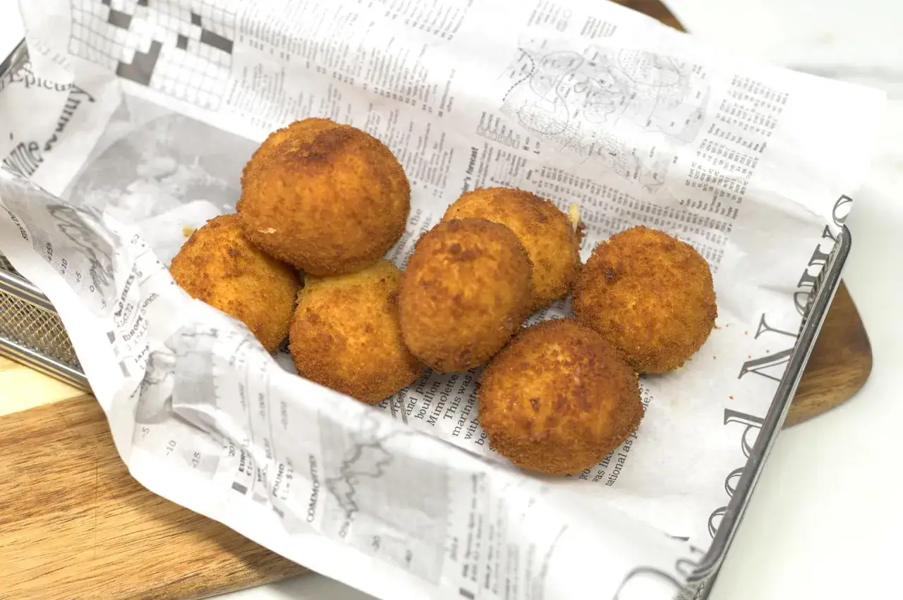 Croquetas de gambas doradas y crujientes, servidas sobre papel de periódico en una cesta metálica.