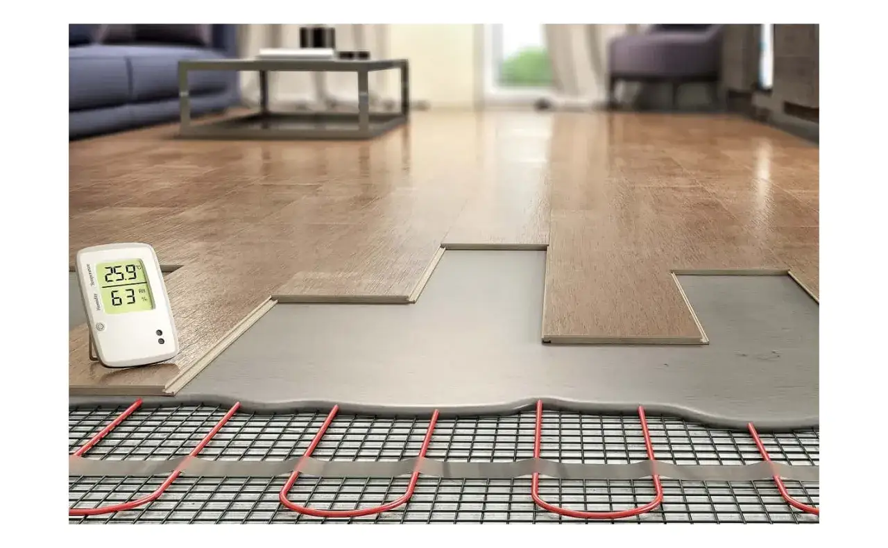 Instalacja ogrzewania w listwach przypodłogowych. Widoczny system grzewczy pod panelami, termometr pokazujący 25.9°C.