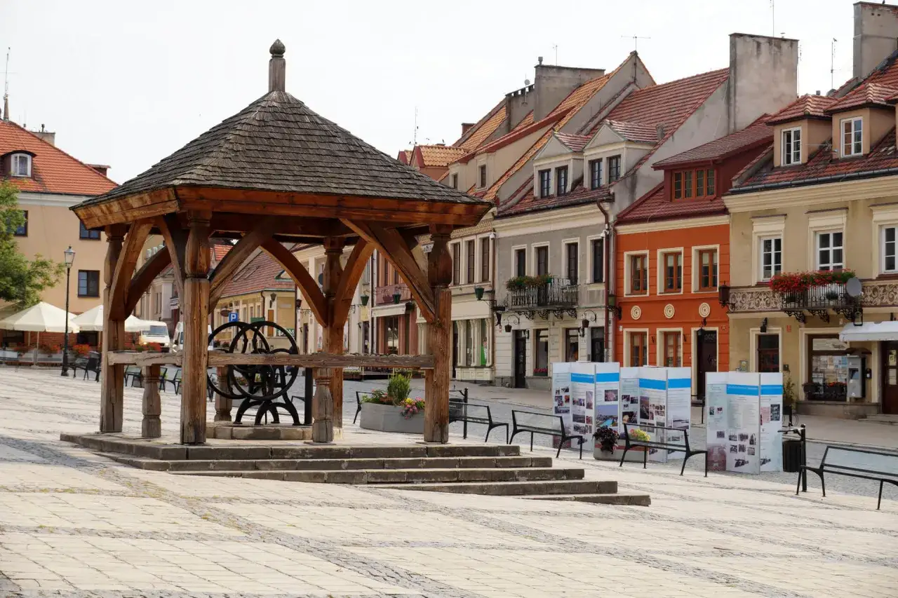 Drewniana studnia na sandomierskim rynku, otoczona kolorowymi kamienicami.