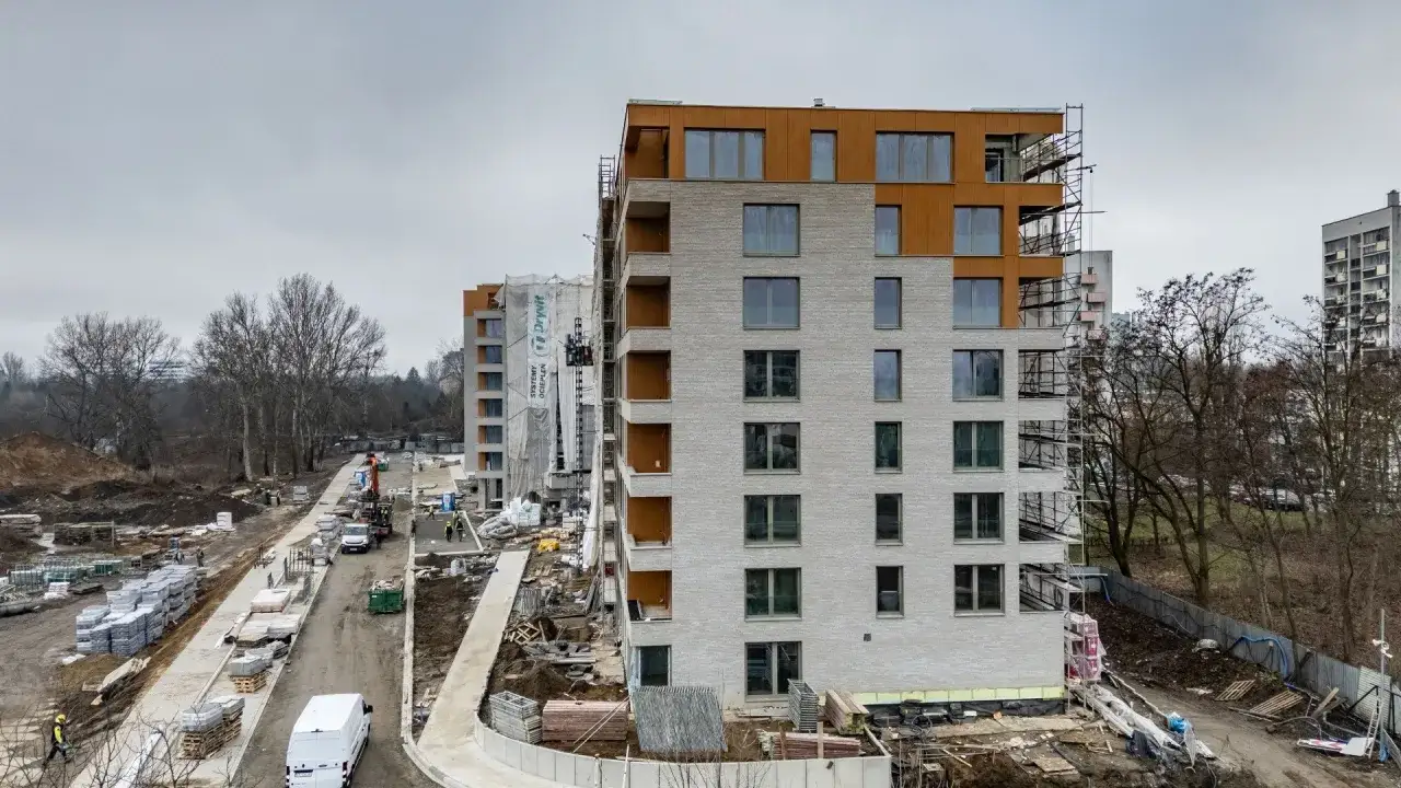 Budowa osiedla mieszkaniowego. Czy warto inwestować w mieszkania? Nowoczesne bloki z drewnianymi elementami, plac budowy z materiałami i maszynami.