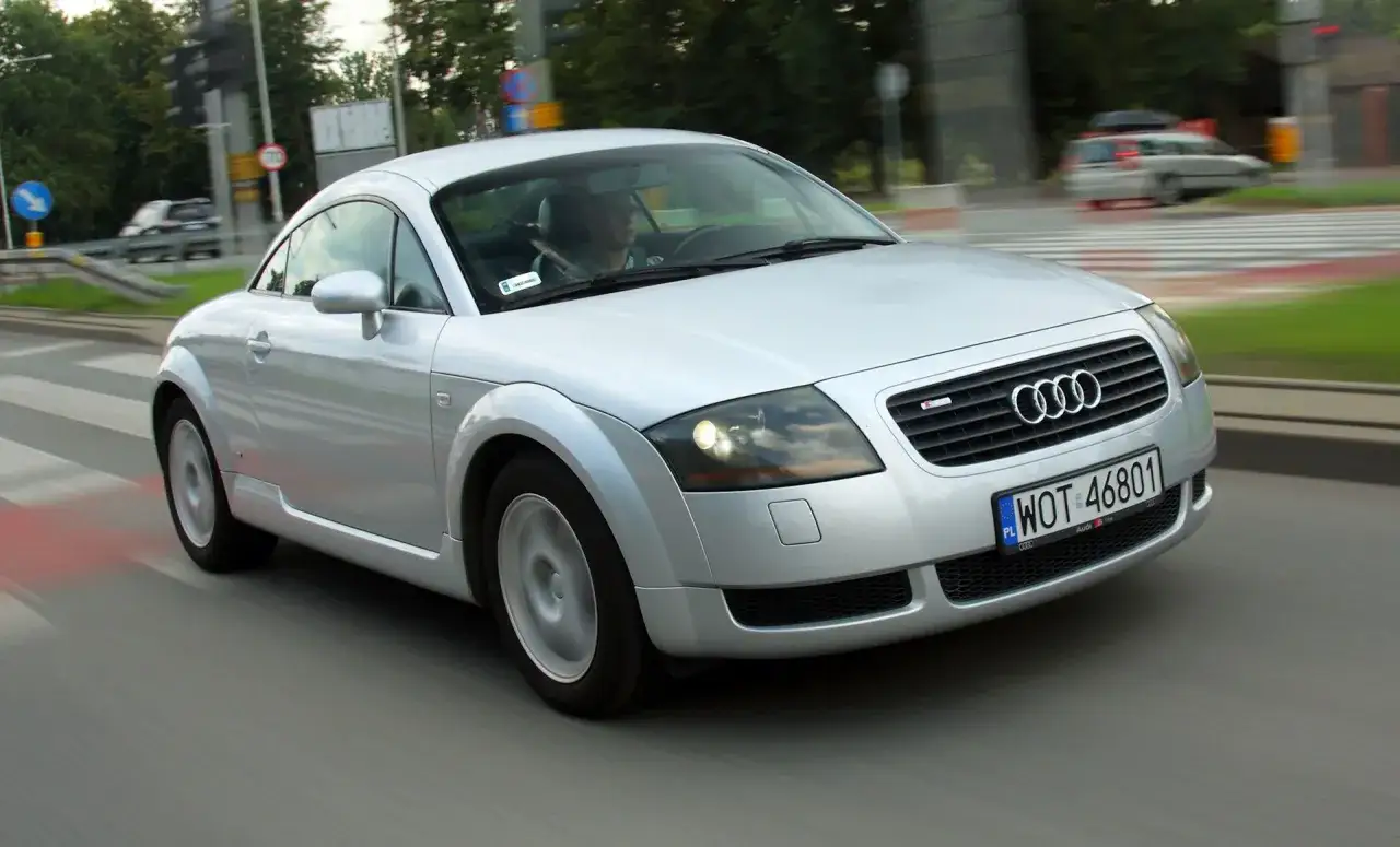 Srebrne Audi TT, jedno z tych tanich sportowych aut, pędzi ulicą.