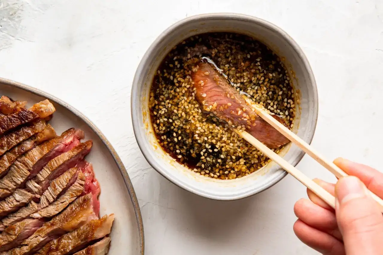 Skivat, saftigt kött doppas i en skål med sesamfrön och sås, perfekt för ett yakiniku recept.