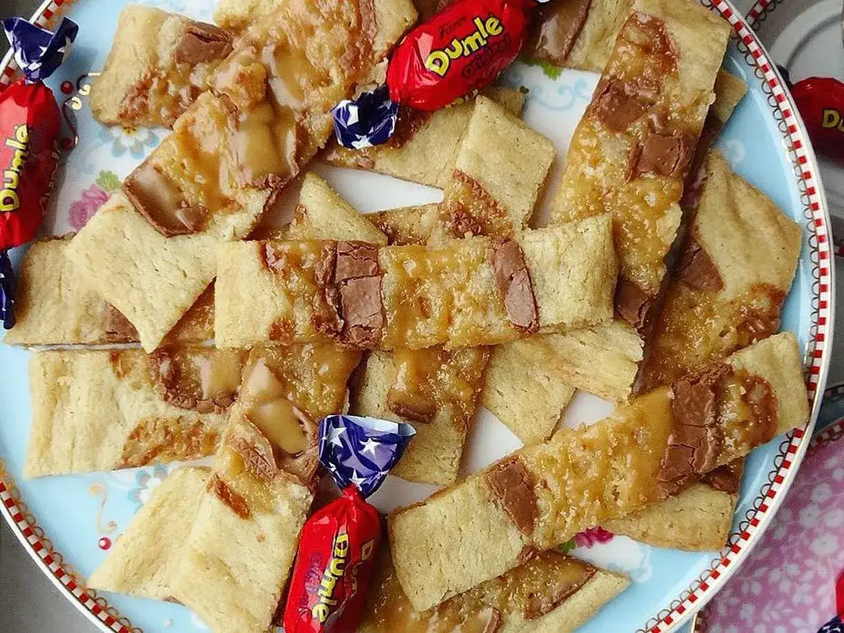 En tallrik med hembakade dumlekakor recept, täckta med smält Dumle och chokladbitar. Några röda Dumle-godisar ligger utspridda.