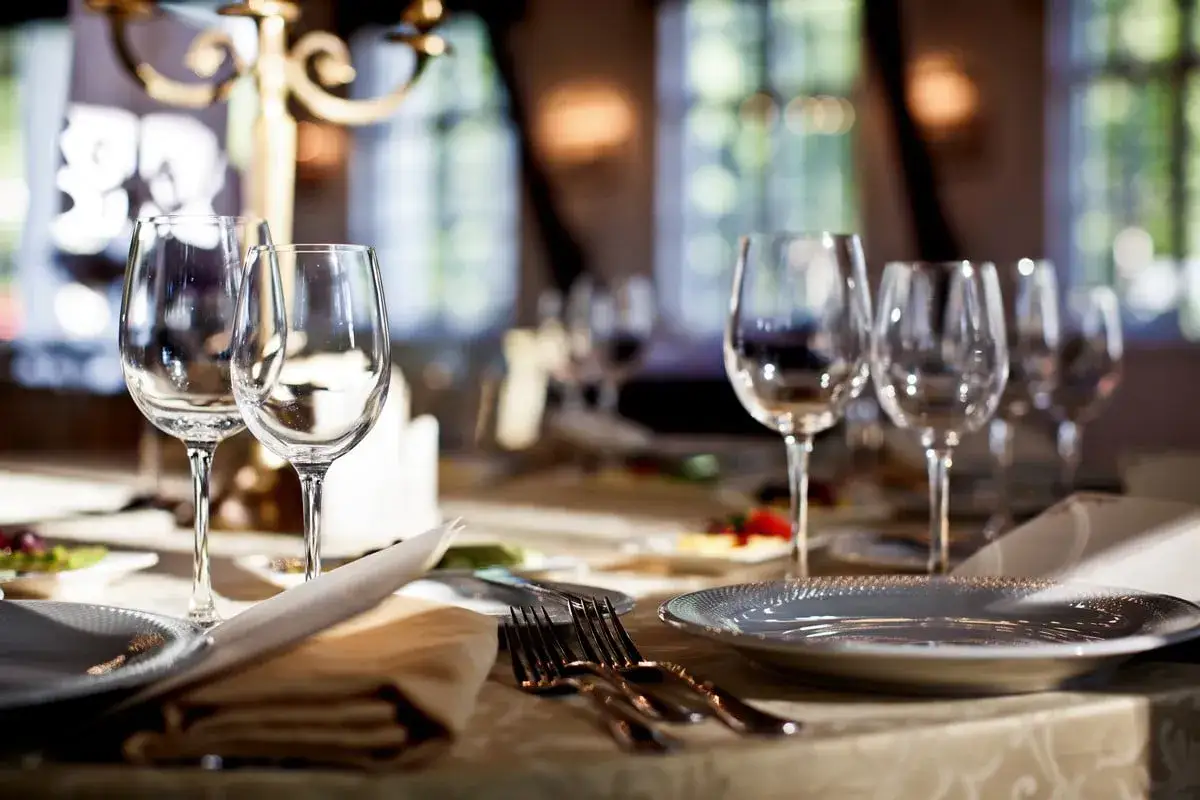 Verres à vin vides et assiettes dressées sur une table élégamment mise, prêts pour un repas. Les art de la table sont à l'honneur.