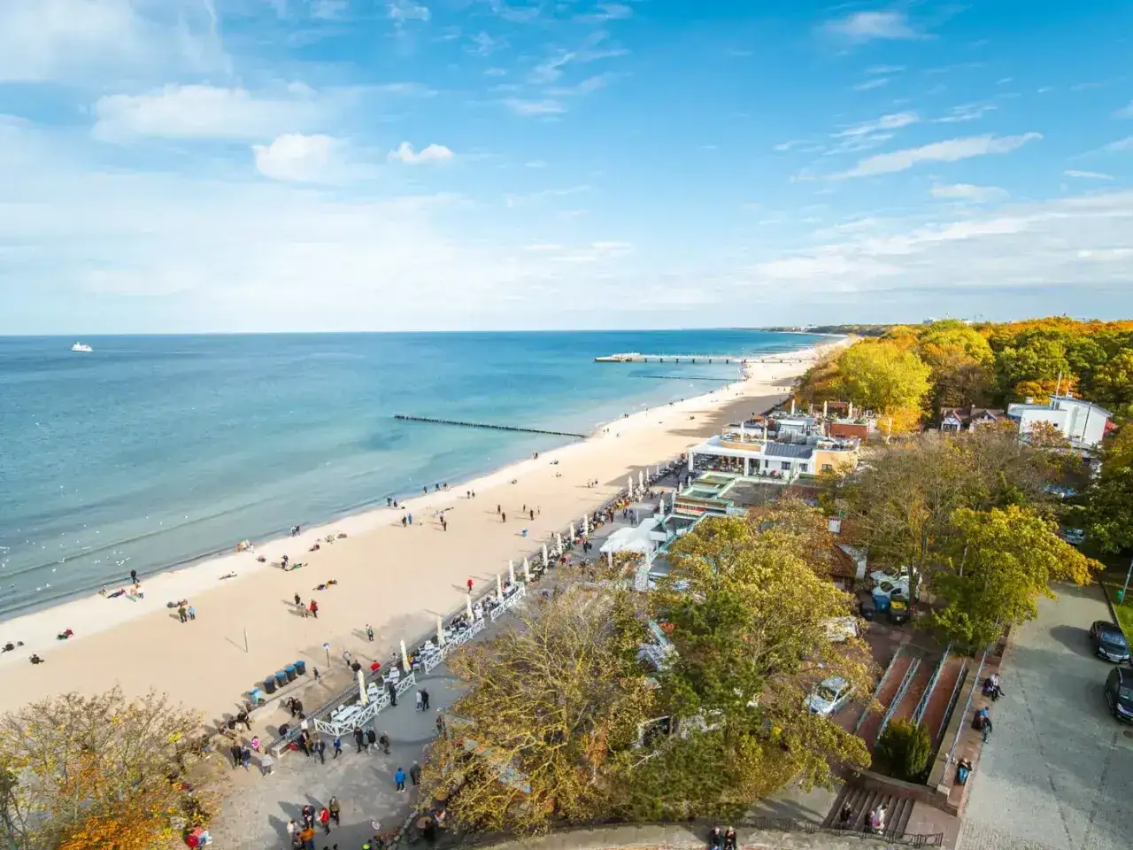 Kołobrzeg atrakcje turystyczne: szeroka plaża, molo, deptak z kawiarniami i jesienne drzewa tworzą malowniczy widok.