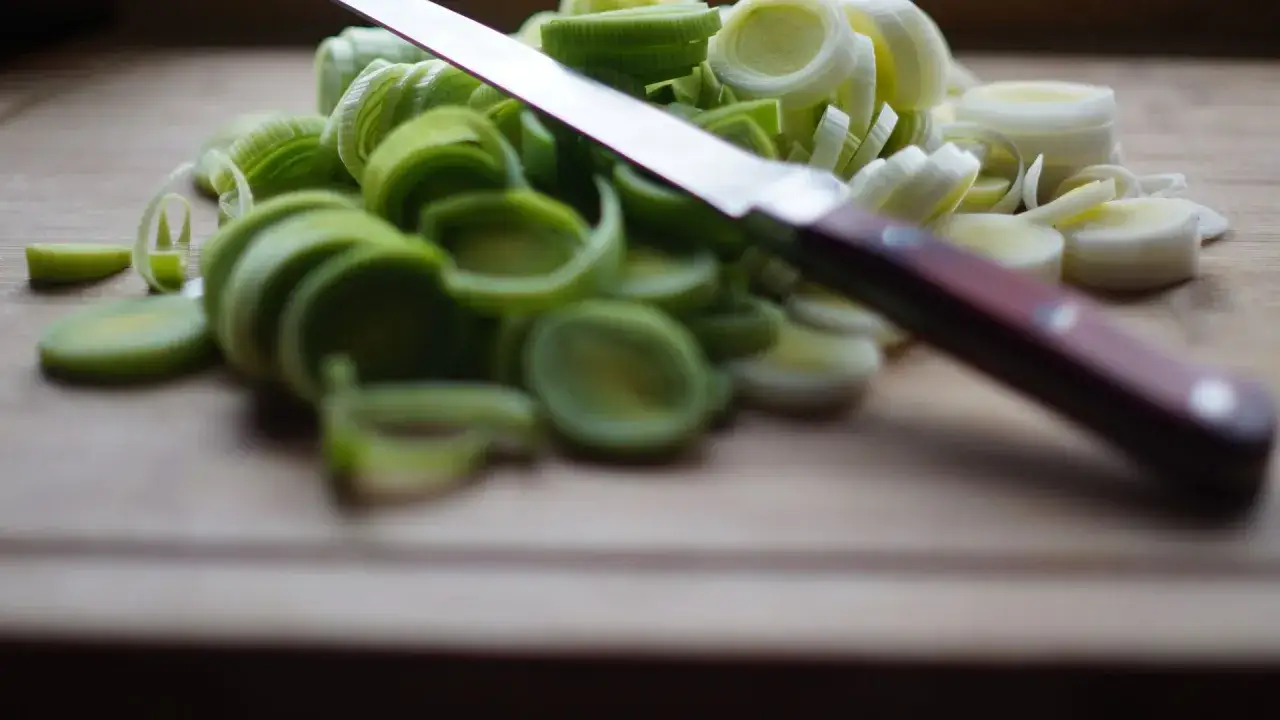 Poireaux coupés en rondelles sur une planche à découper, prêts pour une recette. Un couteau repose sur les légumes verts.