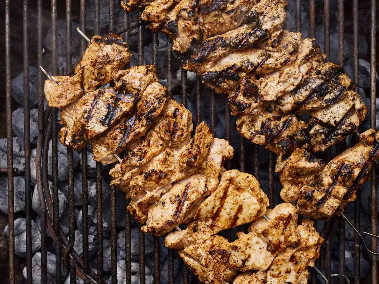 Grillade tavuk sis med h&auml;rliga grillr&auml;nder. Kycklingbitarna ligger p&aring; ett grillgaller &ouml;ver gl&ouml;dande kol.