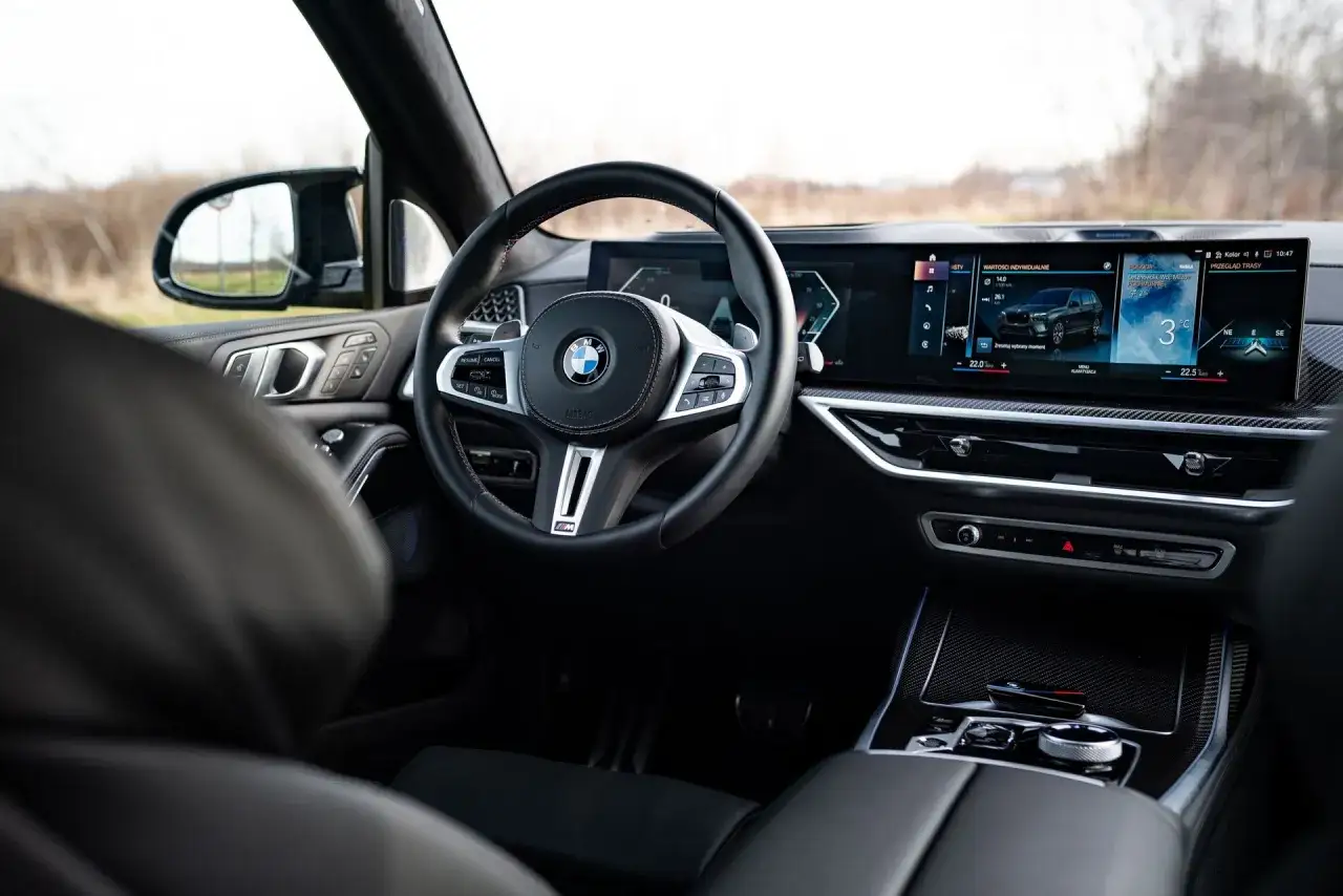 Wnętrze BMW X7 z nowoczesnym kokpitem i dużym ekranem multimedialnym. Kierownica M-Sport i eleganckie wykończenie.