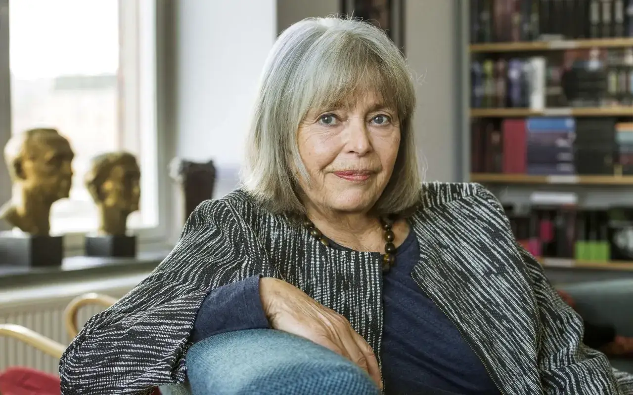 Agneta Pleijel, författare, sitter i en fåtölj med en bokhylla i bakgrunden.