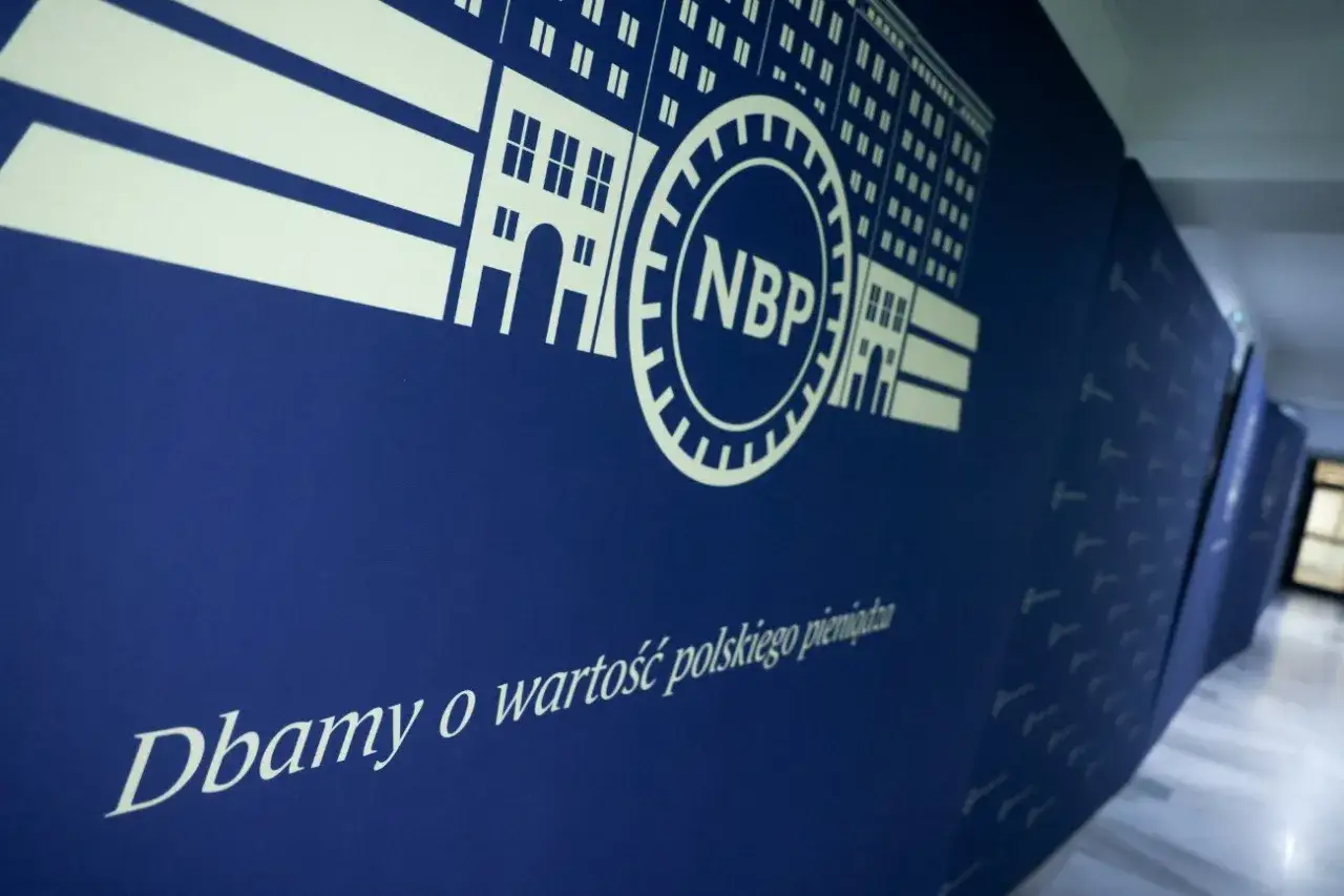 NBP dba o wartość polskiego pieniądza. Na niebieskiej ścianie widnieje logo banku i napis 