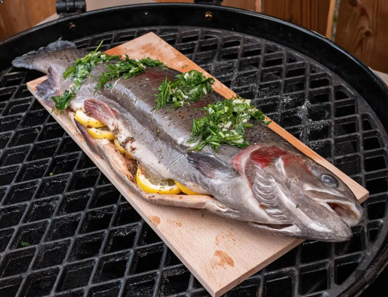 Ein ganzer Fisch mit Zitrone und Kräutern wird auf einem Holzbrett gegrillt.