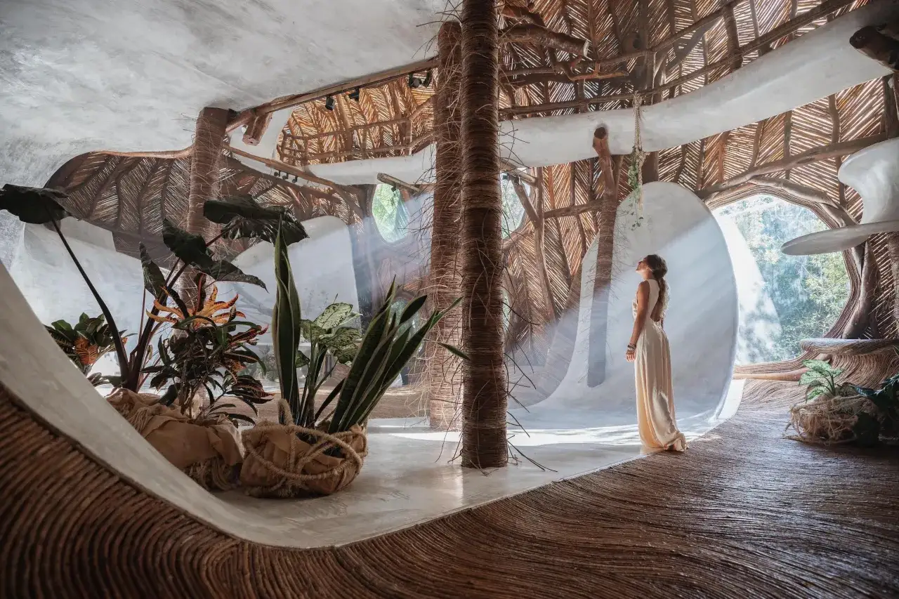 Une femme admire un espace intérieur organique, inspiré par le biomimétisme, avec des piliers en bois tressé et un toit de chaume.