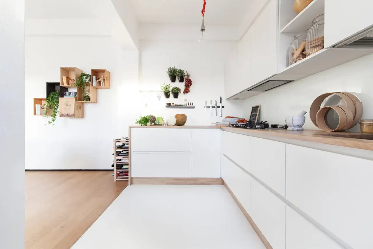 Un progetto cucina angolare piccola, moderna e luminosa con mobili bianchi, piano in legno e mensole decorative.