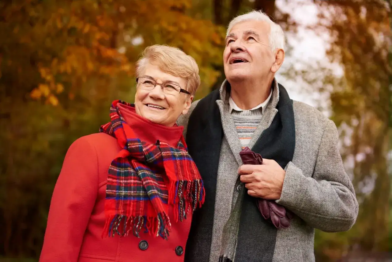 Uśmiechnięci seniorzy w jesiennym parku. Choć czas płynie, nie czują samotności na emeryturze, ciesząc się wspólnymi chwilami.