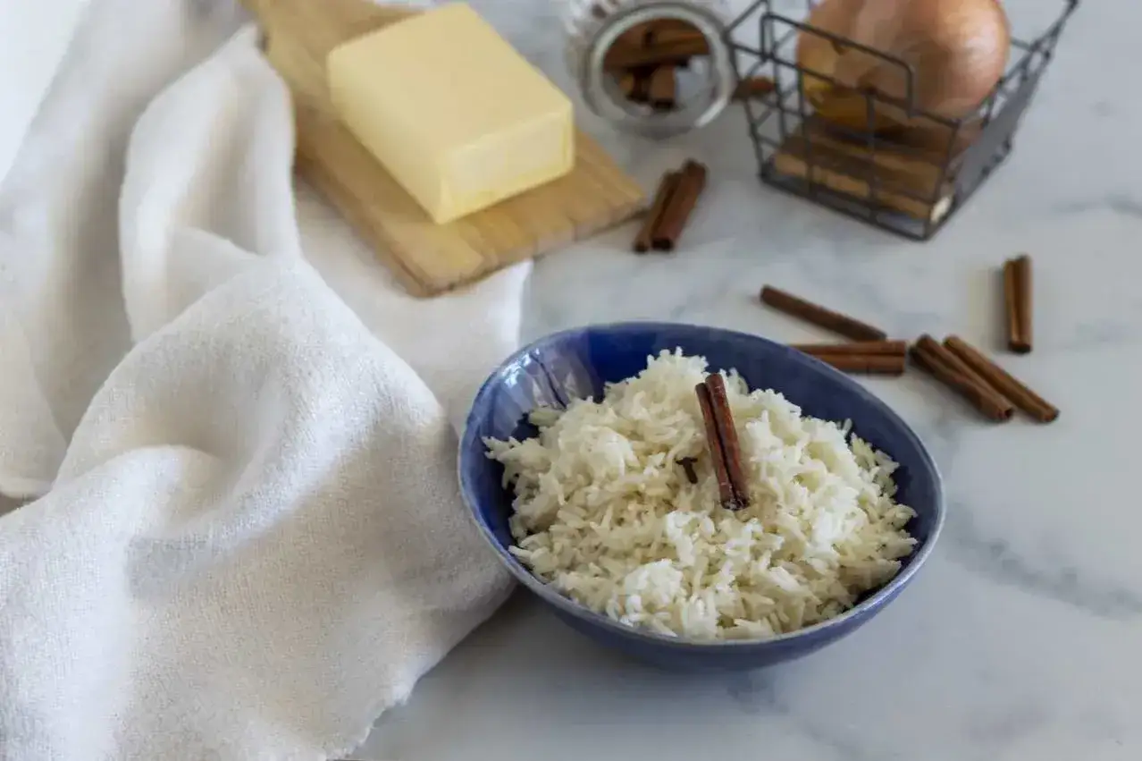 Un profumato riso pilaf in una ciotola blu, con cannella, burro e cipolla sullo sfondo.