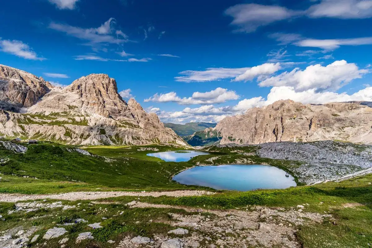 Zwei Bergseen spiegeln den blauen Himmel mit Wolken. Ein idealer Ort f&uuml;r Dolomiten Camping, umgeben von majest&auml;tischen Felsformationen und gr&uuml;nen Almwiesen.