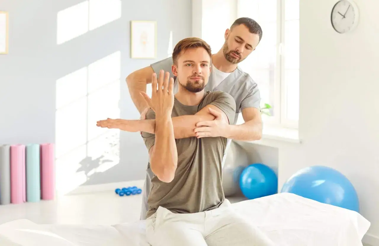 Fizjoterapeuta pomaga pacjentowi w ćwiczeniach rozciągających. To przykład rehabilitacji medycznej.