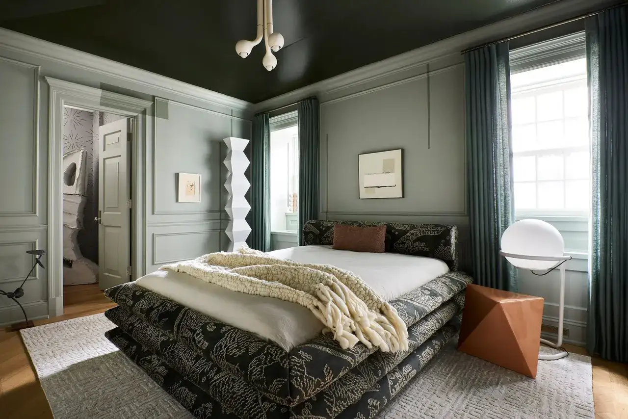 Camera da letto moderna con soffitto verde scuro, un'idea pittura soffitto audace. Letto basso, tessuti ricchi, lampada scultorea.