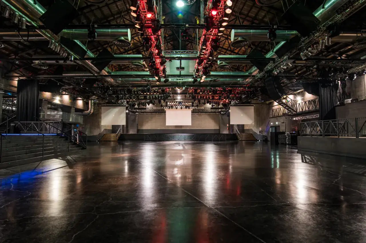 Ampio spazio vuoto con palco e schermi, luci rosse e verdi soffuse, pronto per un evento all'Alcatraz Club Milano.