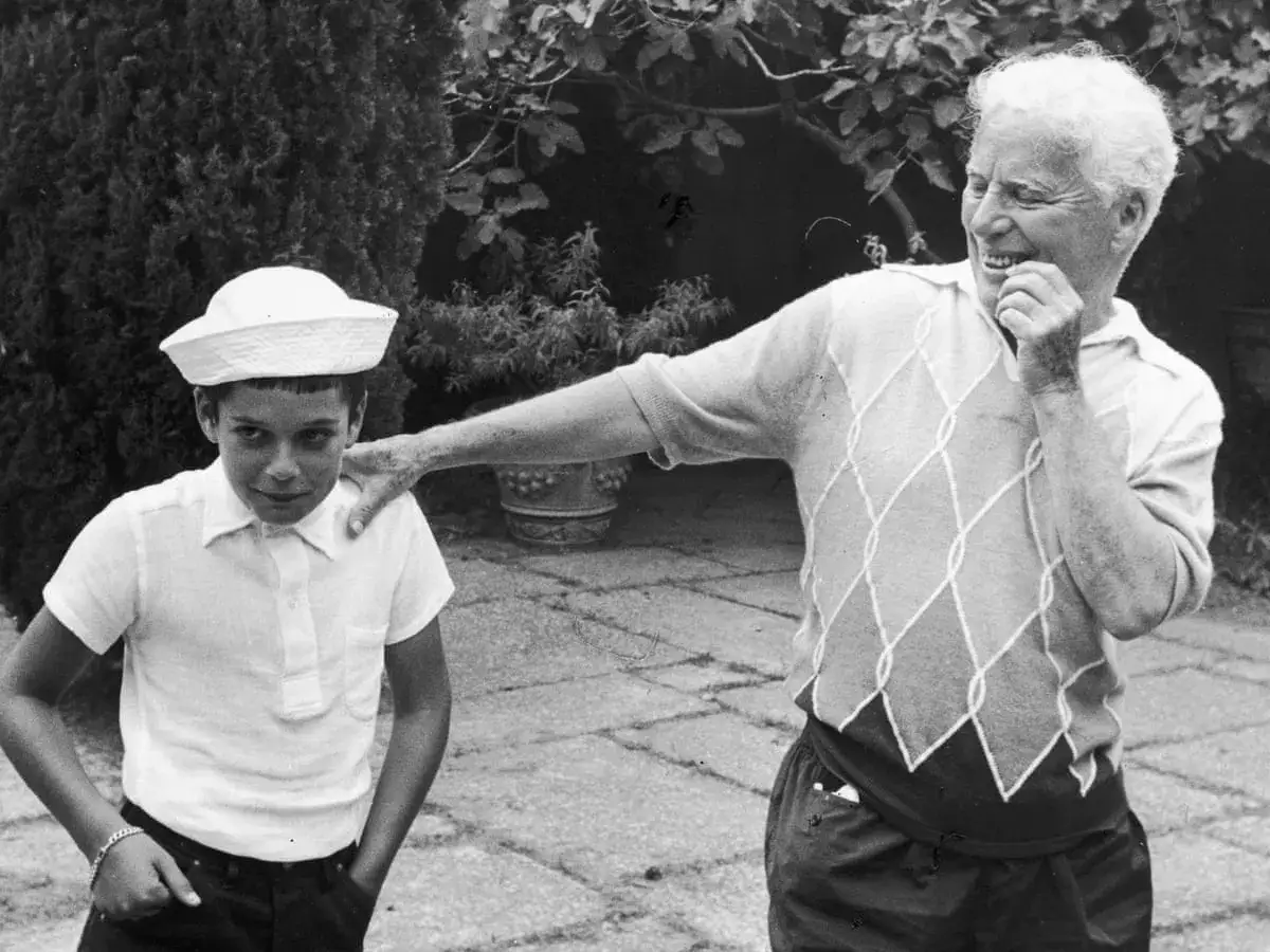 Charlie Chaplin z radością patrzy na jednego ze swoich dzieci, chłopca w białej marynarskiej czapce.
