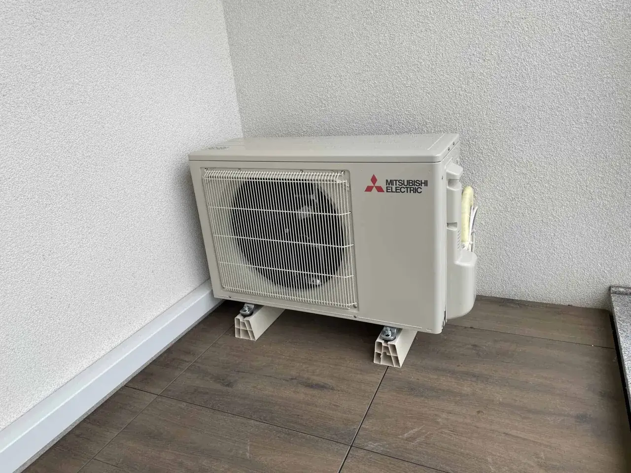 Jednostka zewnętrzna klimatyzatora Mitsubishi Electric na drewnianej podłodze.