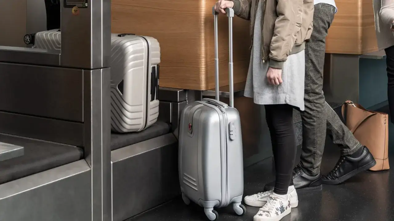 Person med handbagage fr&aring;n Austrian Airlines vid incheckningen. Silverf&auml;rgad kabinv&auml;ska med hjul.