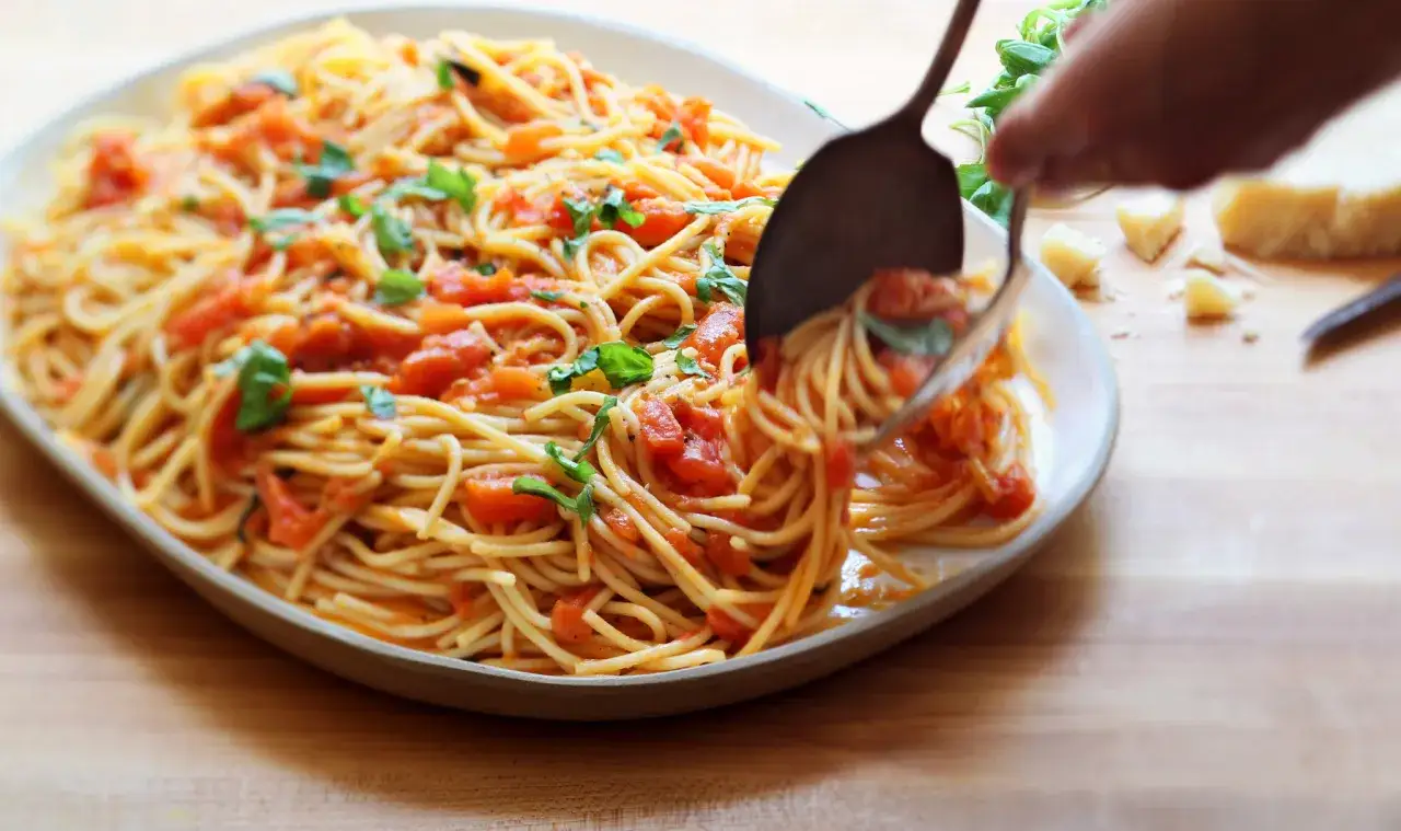 En stor portion pasta med tomatsås och färsk basilika, som serveras med en bit parmesanost.