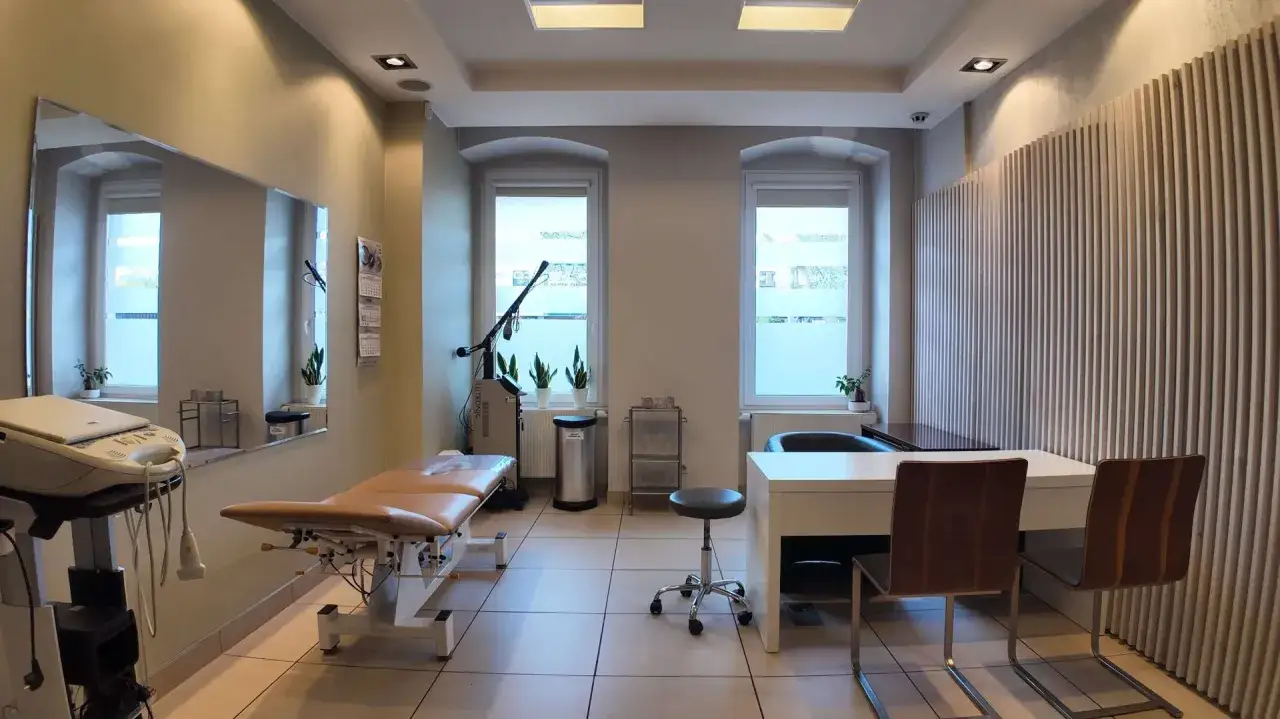 Gabinet medyczny z kozetką, biurkiem, lustrem i oknami.