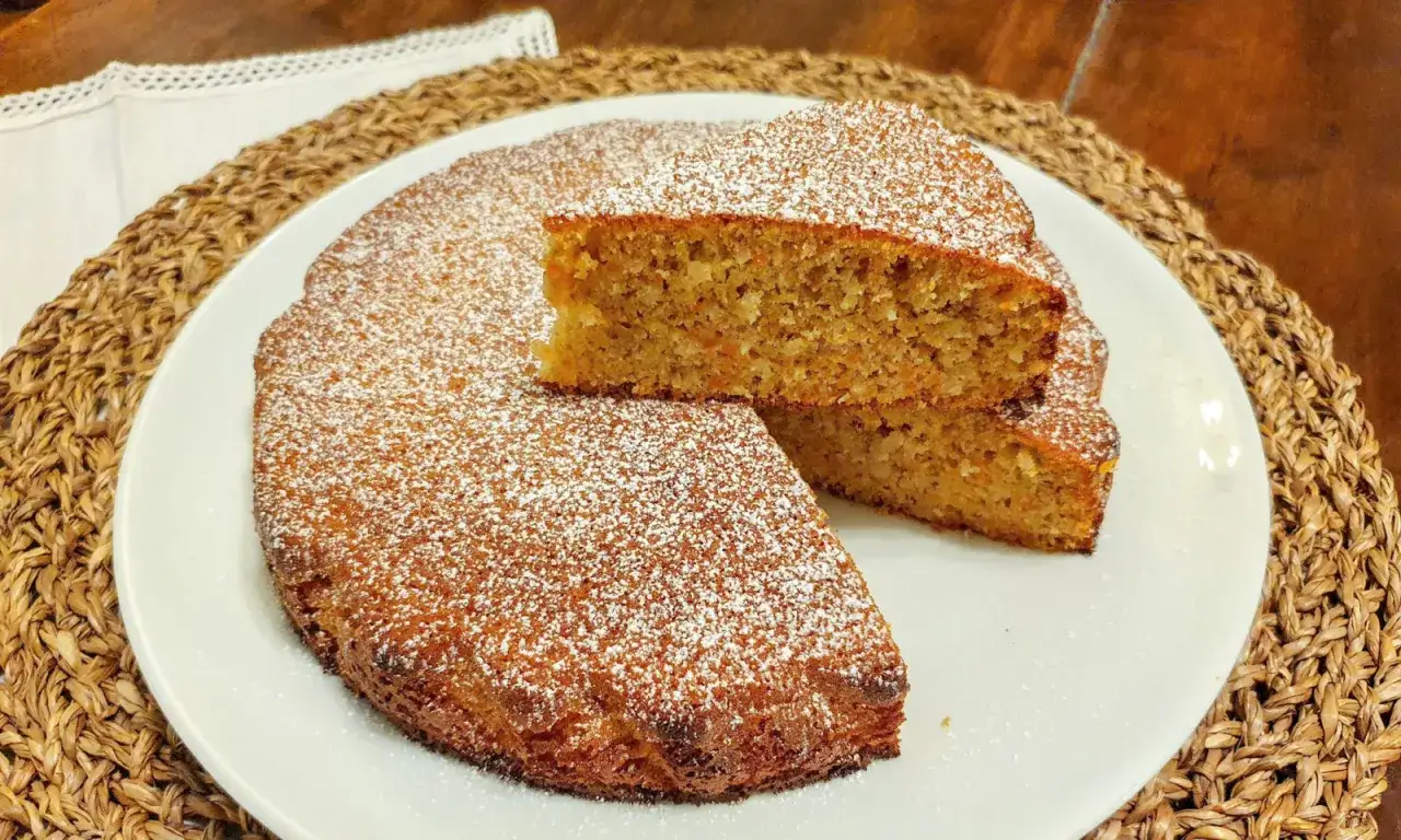 Una deliziosa torta carote e mandorle, cosparsa di zucchero a velo, servita su un piatto bianco.