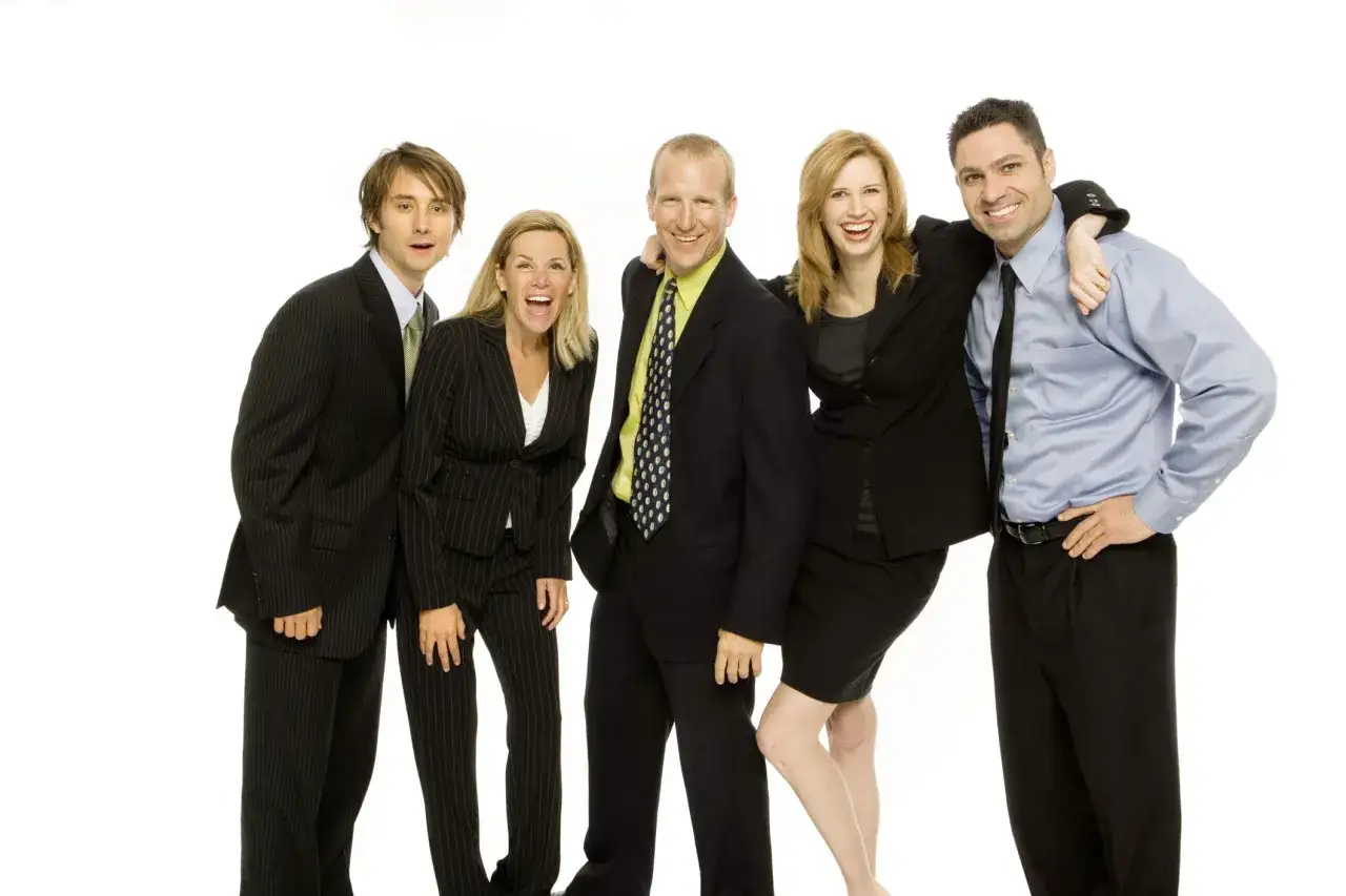A diverse team celebrates, showcasing great employee recognition examples. They are laughing and posing together in business attire.