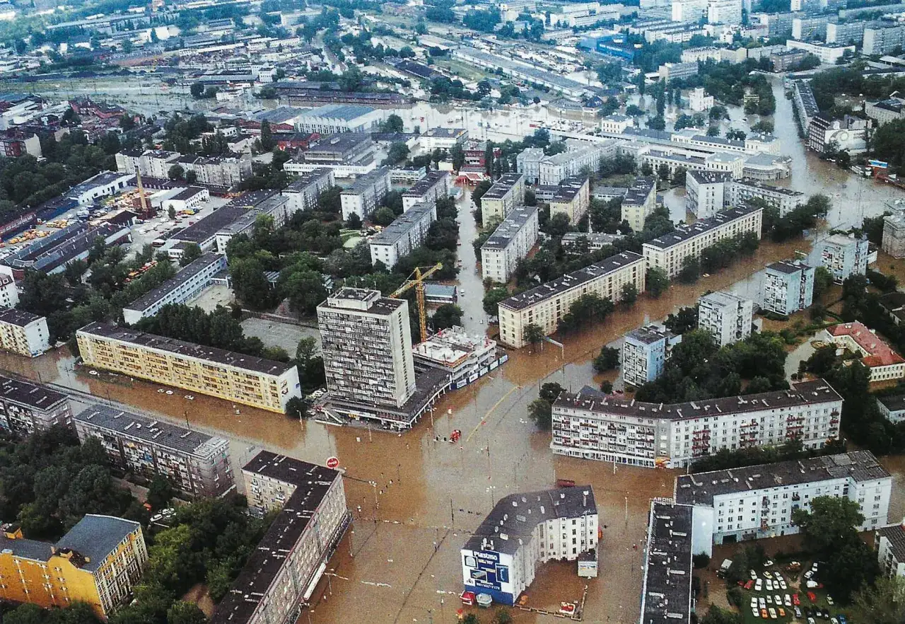 Powódź 1997. Zalane ulice i budynki mieszkalne w mieście. Woda sięga do pierwszych pięter, a na ulicach widać łodzie ratunkowe.