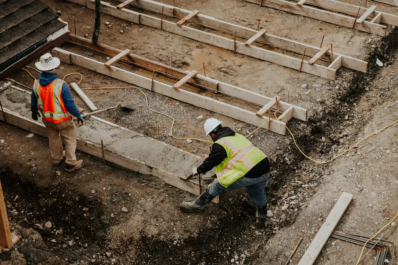 Pracownicy budowlani w kamizelkach odblaskowych wylewają beton. Zastanawiasz się, ile kosztują fundamenty?