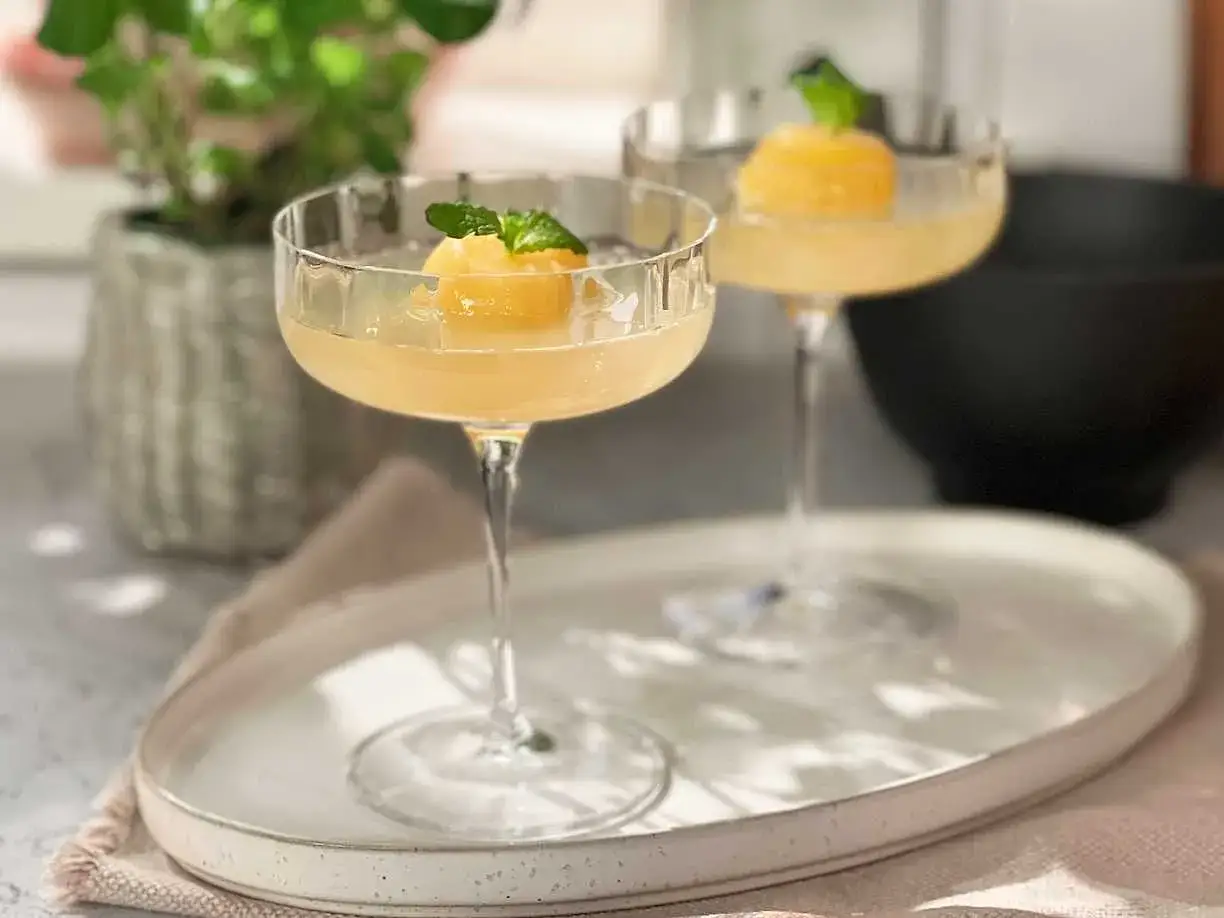 Tv&aring; eleganta glas med en ljusgul mimosa drink, toppad med en persikokula och mynta. Perfekt f&ouml;r en solig brunch.