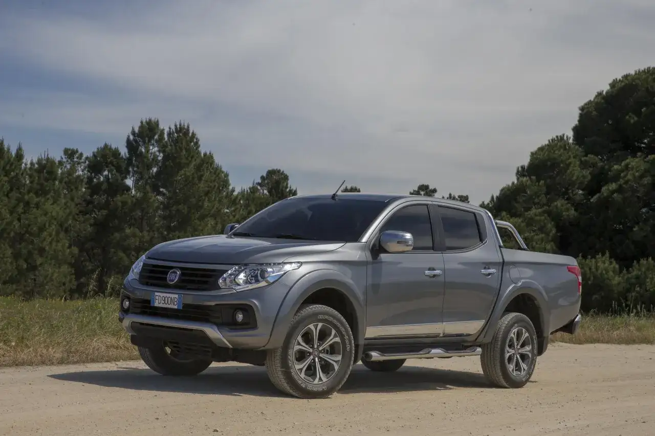 Szary Fiat Fullback na drodze gruntowej, otoczony drzewami.