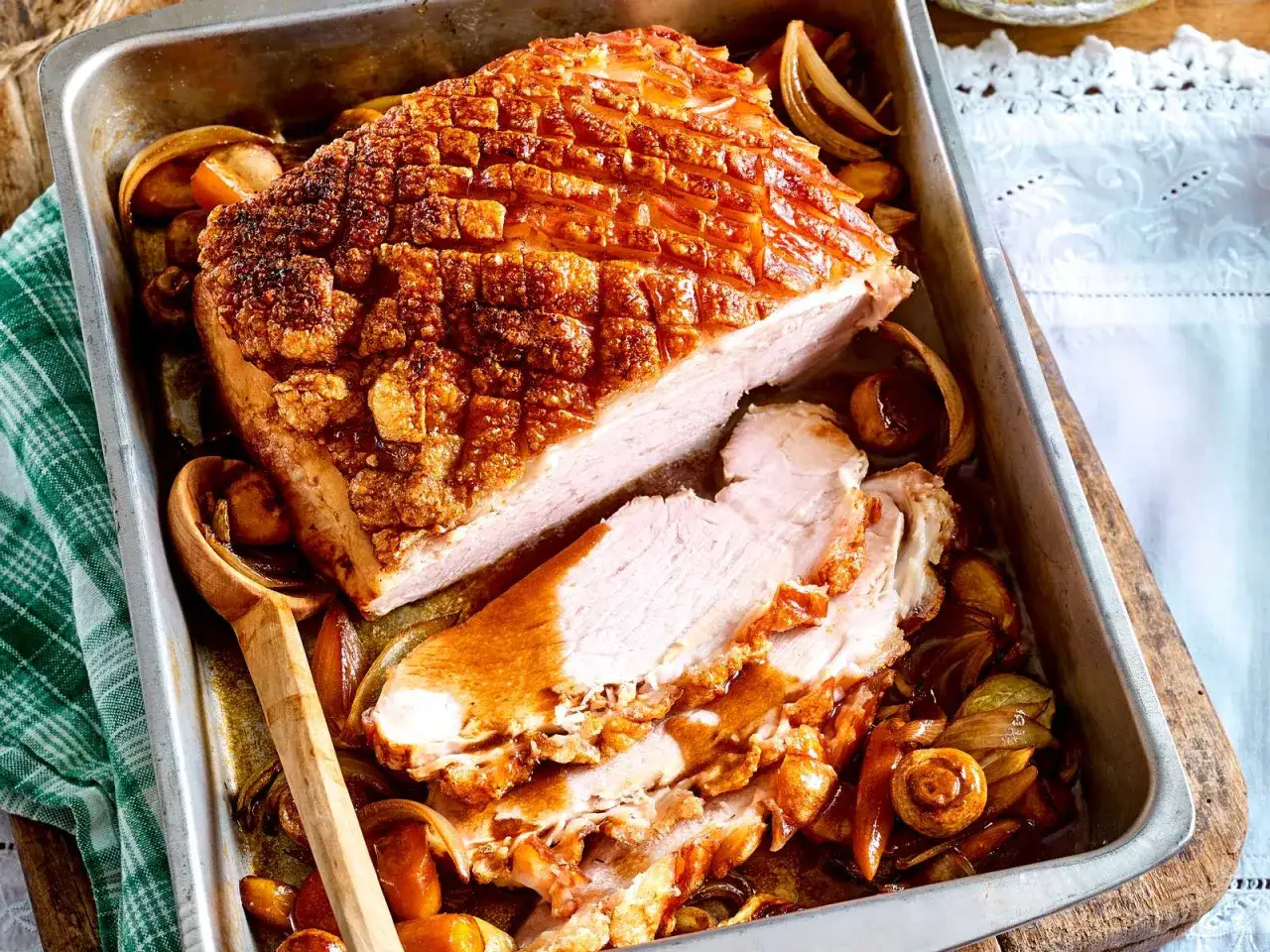 Saftiger schweineschulterbraten mit knuspriger Schwarte, serviert mit karamellisierten Zwiebeln und Pilzen in einer Bratpfanne.