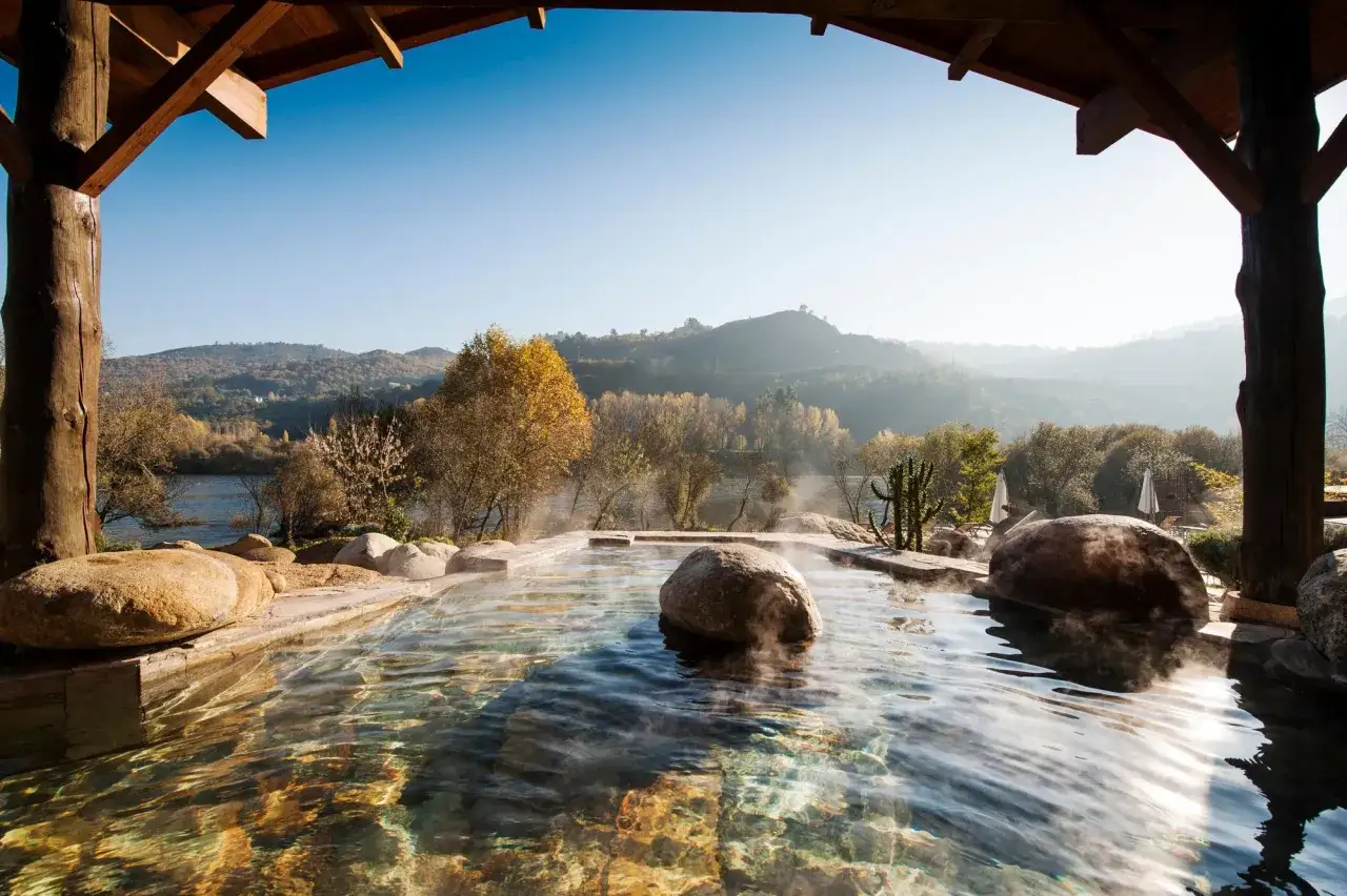 Relájate en estas termas en Galicia, con vapor ascendiendo del agua cristalina y un paisaje montañoso de fondo.
