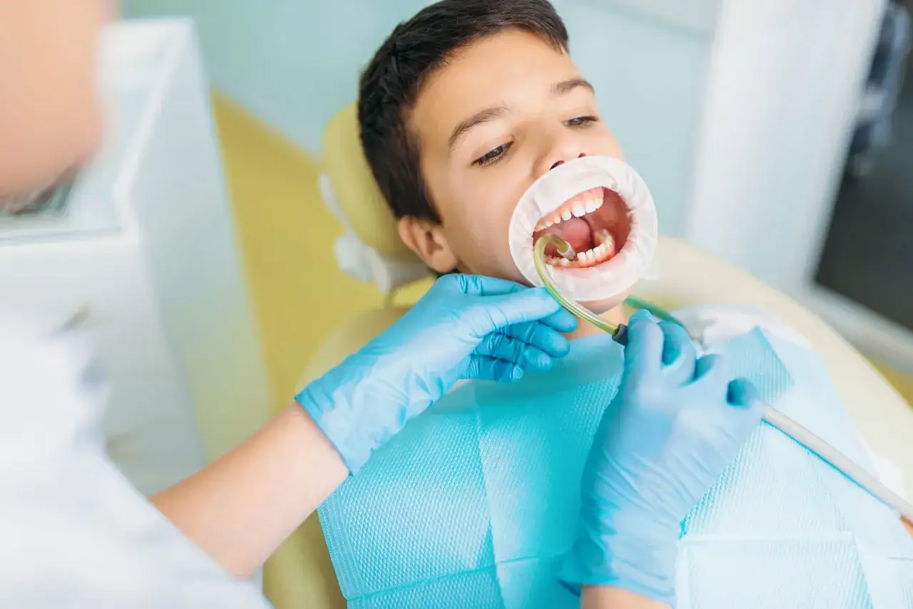Chłopiec z rozchylonymi ustami, u dentysty. Widoczne mleczne zęby, które mogą być zagrożone próchnicą.