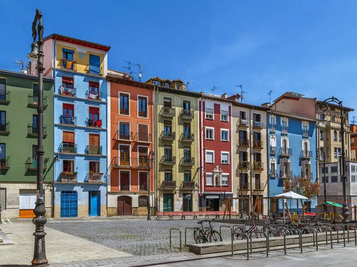 Fachada de edificios coloridos en una plaza, ideal para saber qué ver en Pamplona. Hay bicicletas aparcadas y un parque infantil.