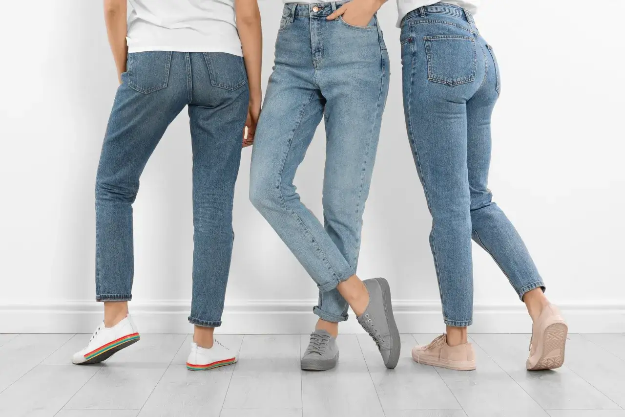 Trzy kobiety w jeansach i sneakersach. Dowiedz się, jak rozciągnąć jeansy, by były idealnie dopasowane.