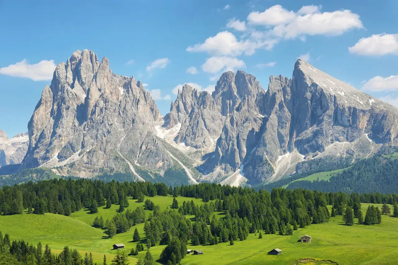 Iconiche cime rocciose dominano un paesaggio alpino con prati verdi e boschi, un classico tra le località di montagna famose.