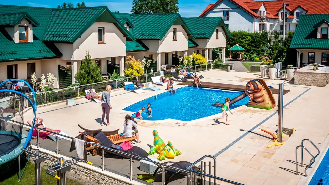 Rodzinny wypoczynek w domkach apartamentowych Fulay Premium. Dzieci bawią się w basenie, dorośli relaksują się na leżakach.