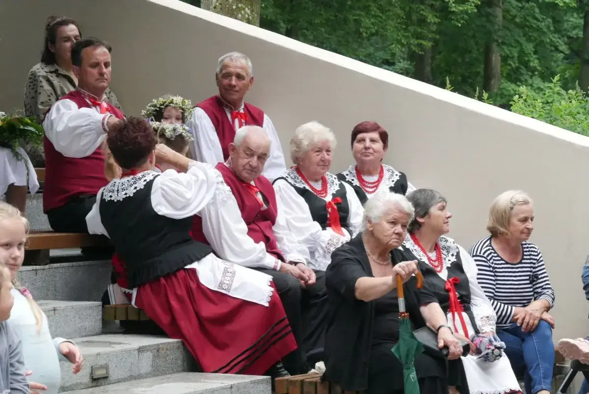 Ludzie w strojach ludowych, przygotowujący się do pieśni świętojańskiej o sobótce. Wianek na głowie dziewczynki.